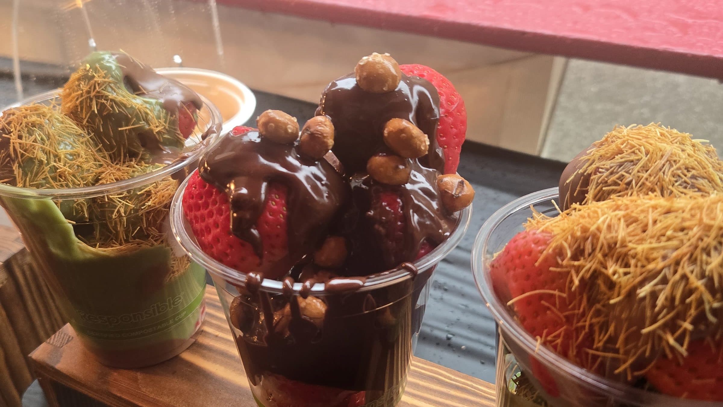 Cups of chocolate-covered strawberries topped with pistachio cream and toasted kanafe