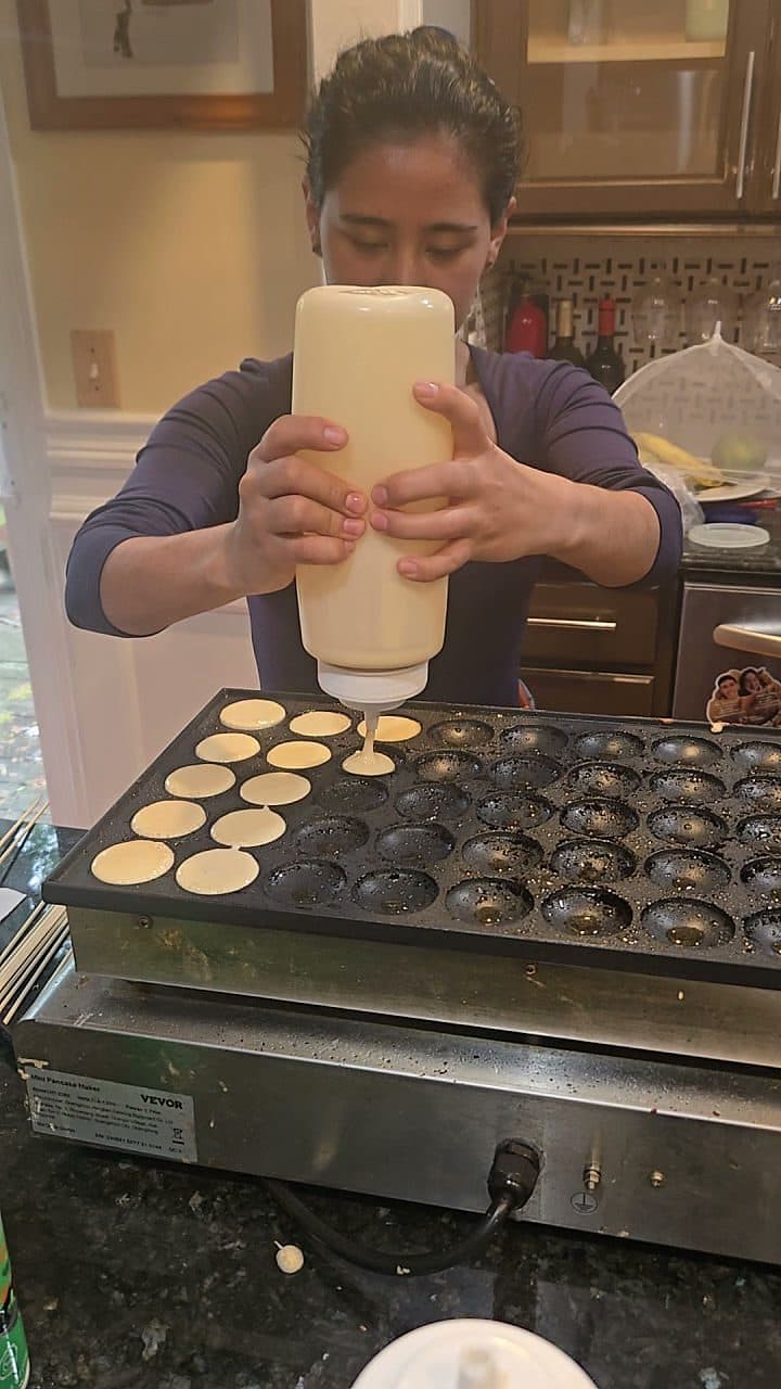 Pouring fresh batter into a traditional poffertjes griddle