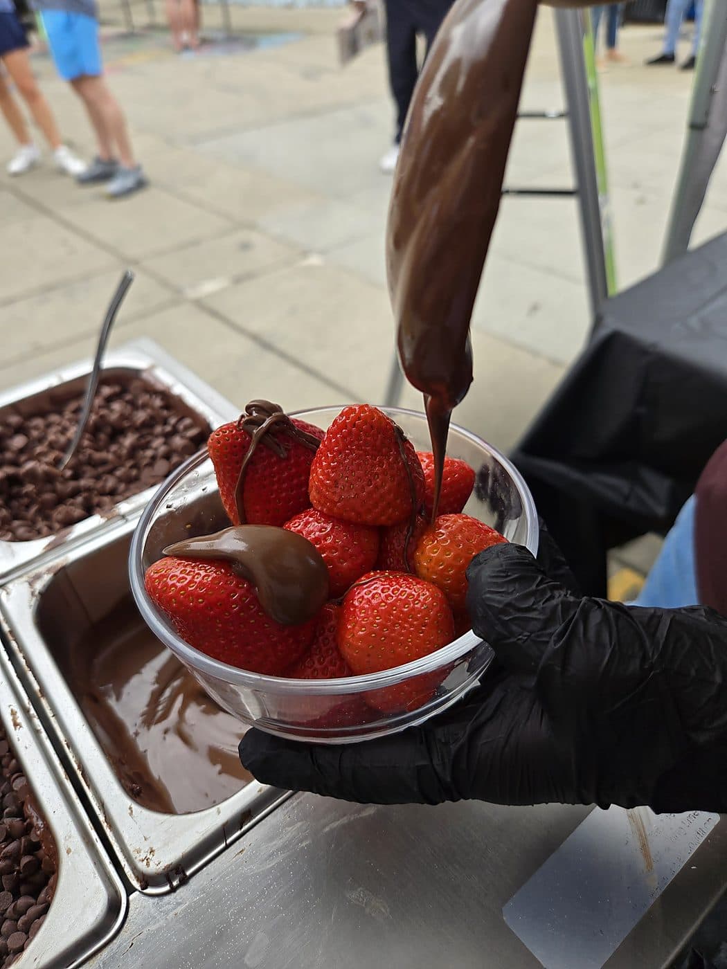 A fresh strawberry being coated in melted chocolate over the dipping tray