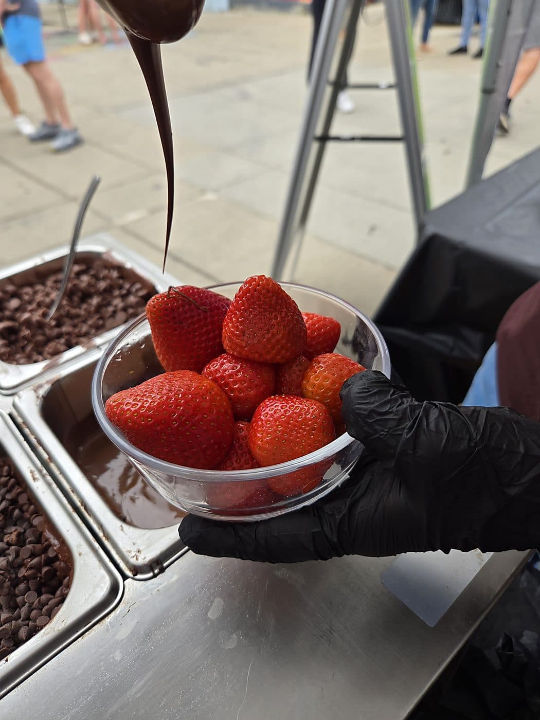 Chocolate pouring from a piping bag over a bowl of fresh strawberries