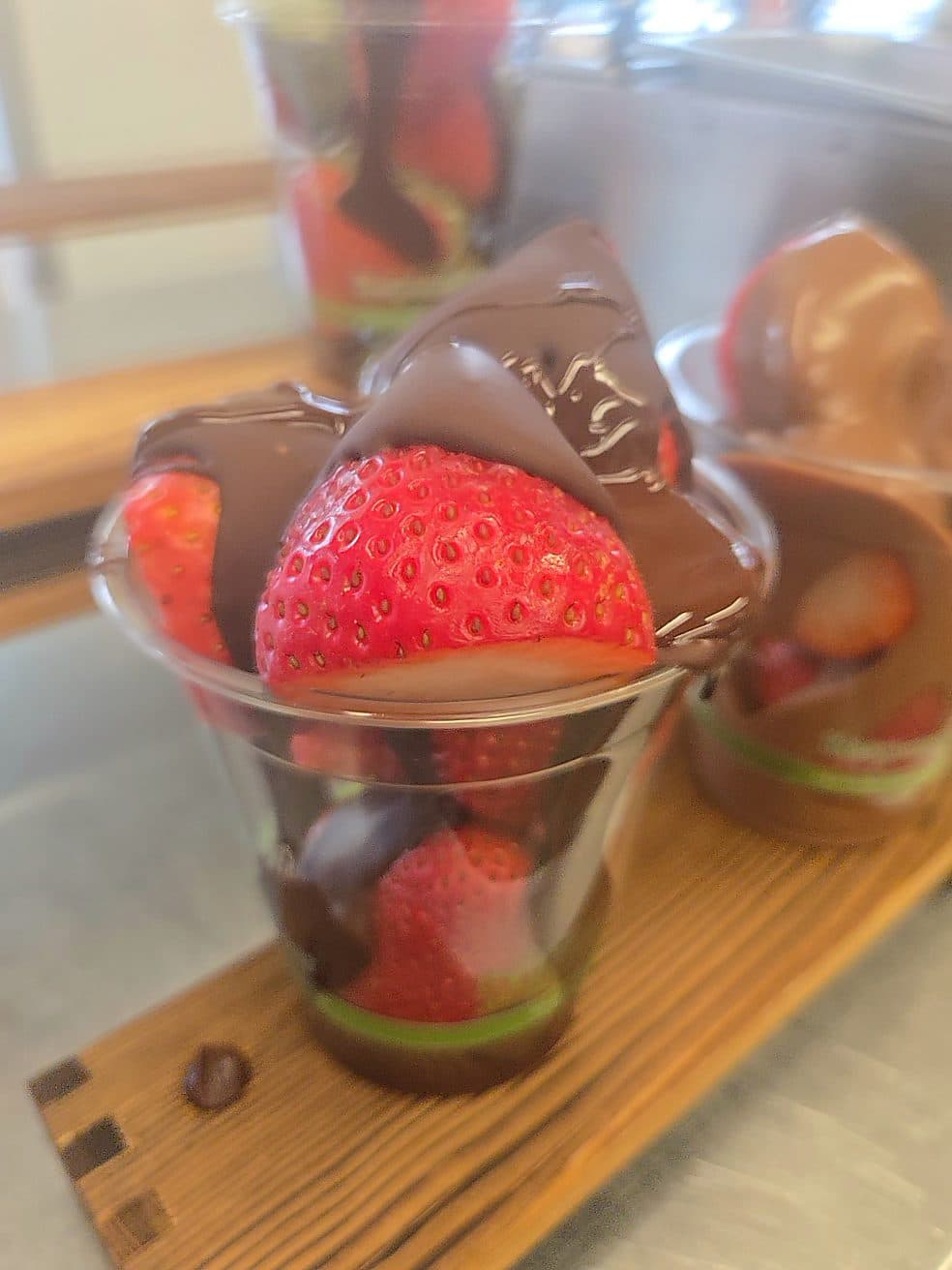 Chocolate-covered strawberries served in a clear cup on a wooden board