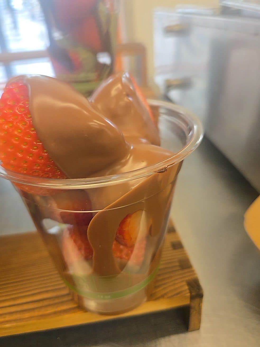 A fresh strawberry coated in premium milk chocolate, served in a cup