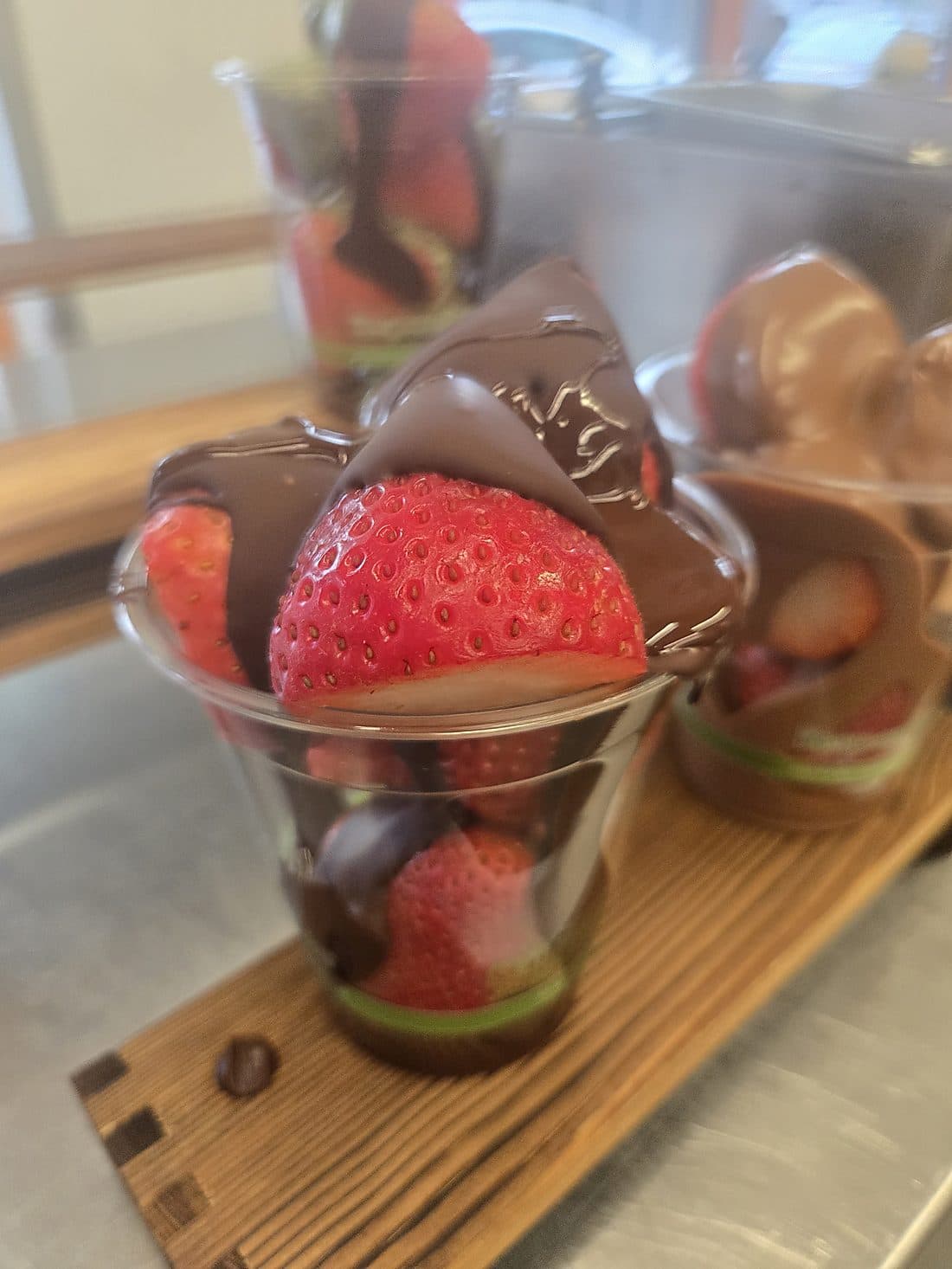 Dark chocolate-covered strawberries served in cups on a wooden serving board