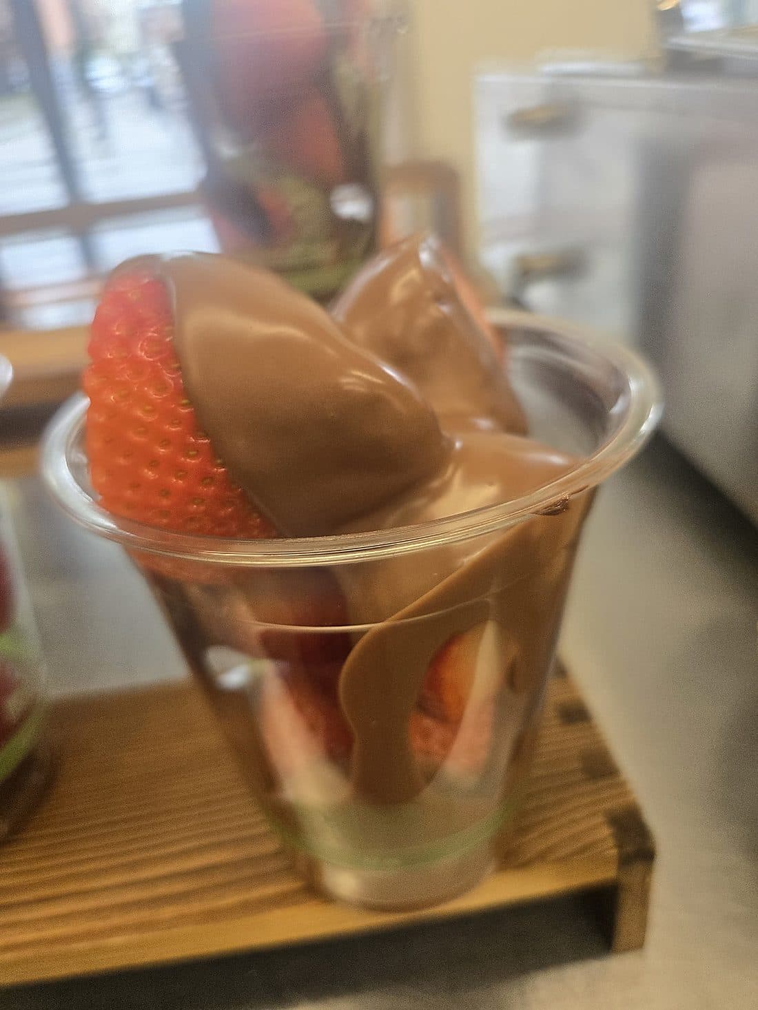 A fresh strawberry dipped in premium milk chocolate served in a clear cup