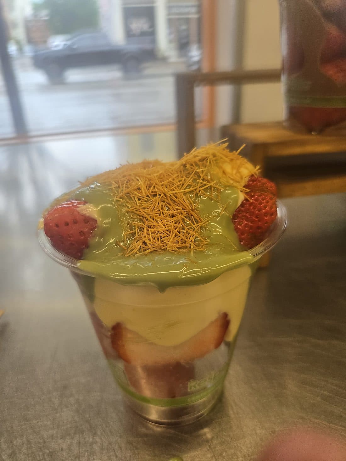 A layered pistachio cream and strawberry cup finished with golden toasted kanafe